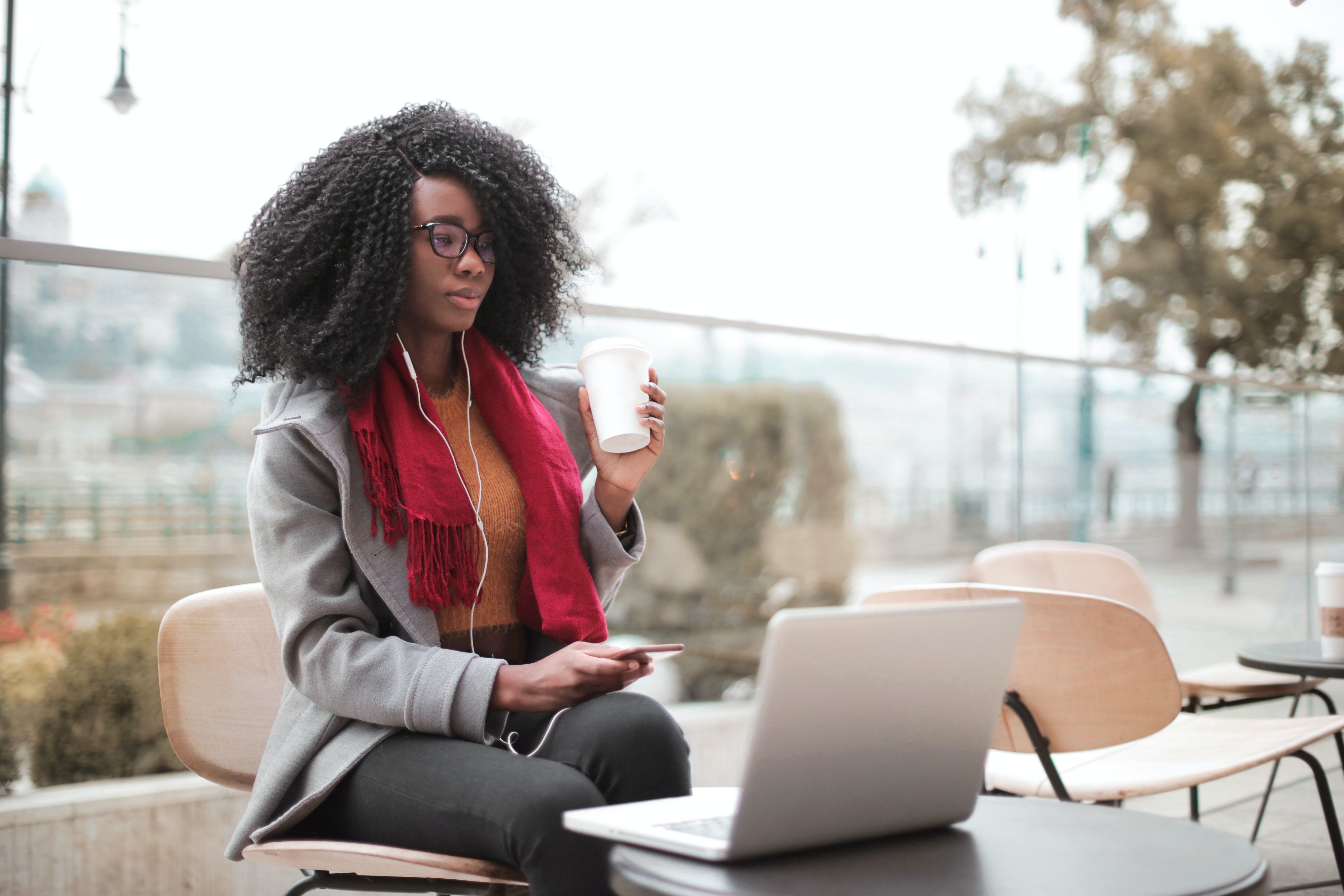 Woman enjoying a peaceful outdoor workspace with her laptop, savoring a cup of coffee and staying connected with her earphones.