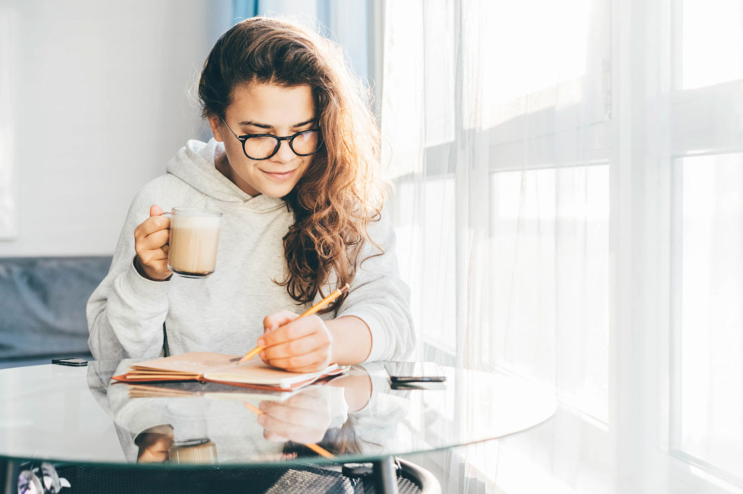 Woman enjoying a cup of coffee while engaging in journaling activities.